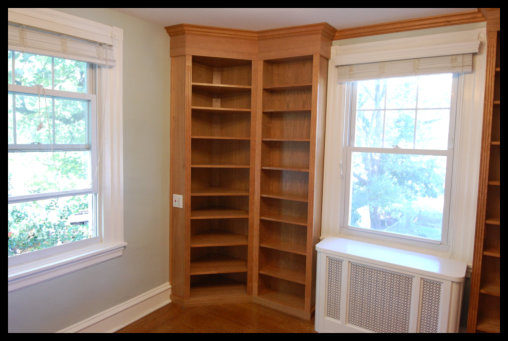 Double-wide 45 degree cherry corner bookcase; floor-to-ceiling open-face shelving with custom crown molding.