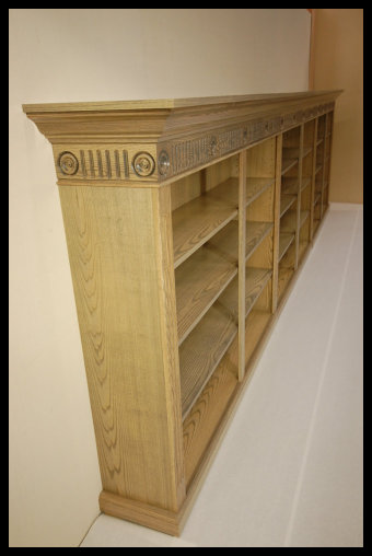 A 20-foot custom modular bookcase handcrafted in three sections for portability, featuring fluted moldings, decorative rosettes, and a solid wood tabletop.